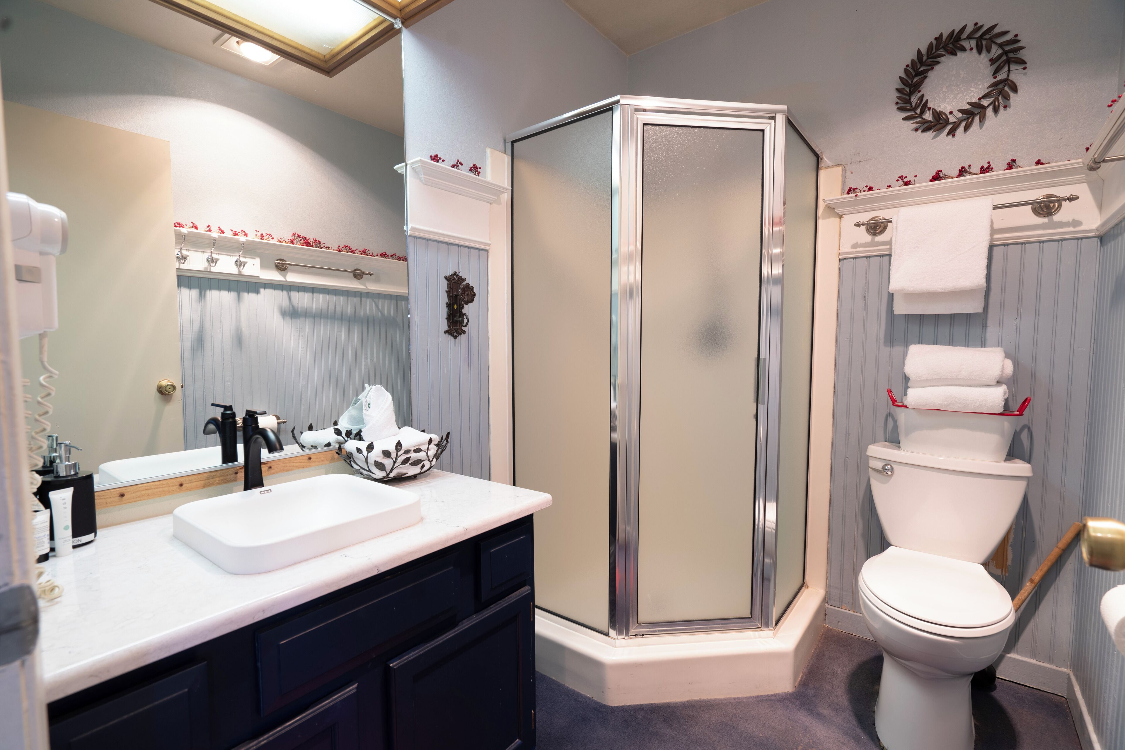 A bathroom with a white sink, dark cabinets, a glass shower enclosure, and a toilet with a towel rack.