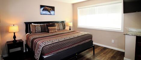 A bedroom with a large bed, two bedside tables with lamps, a wall-mounted TV, and a window with blinds.