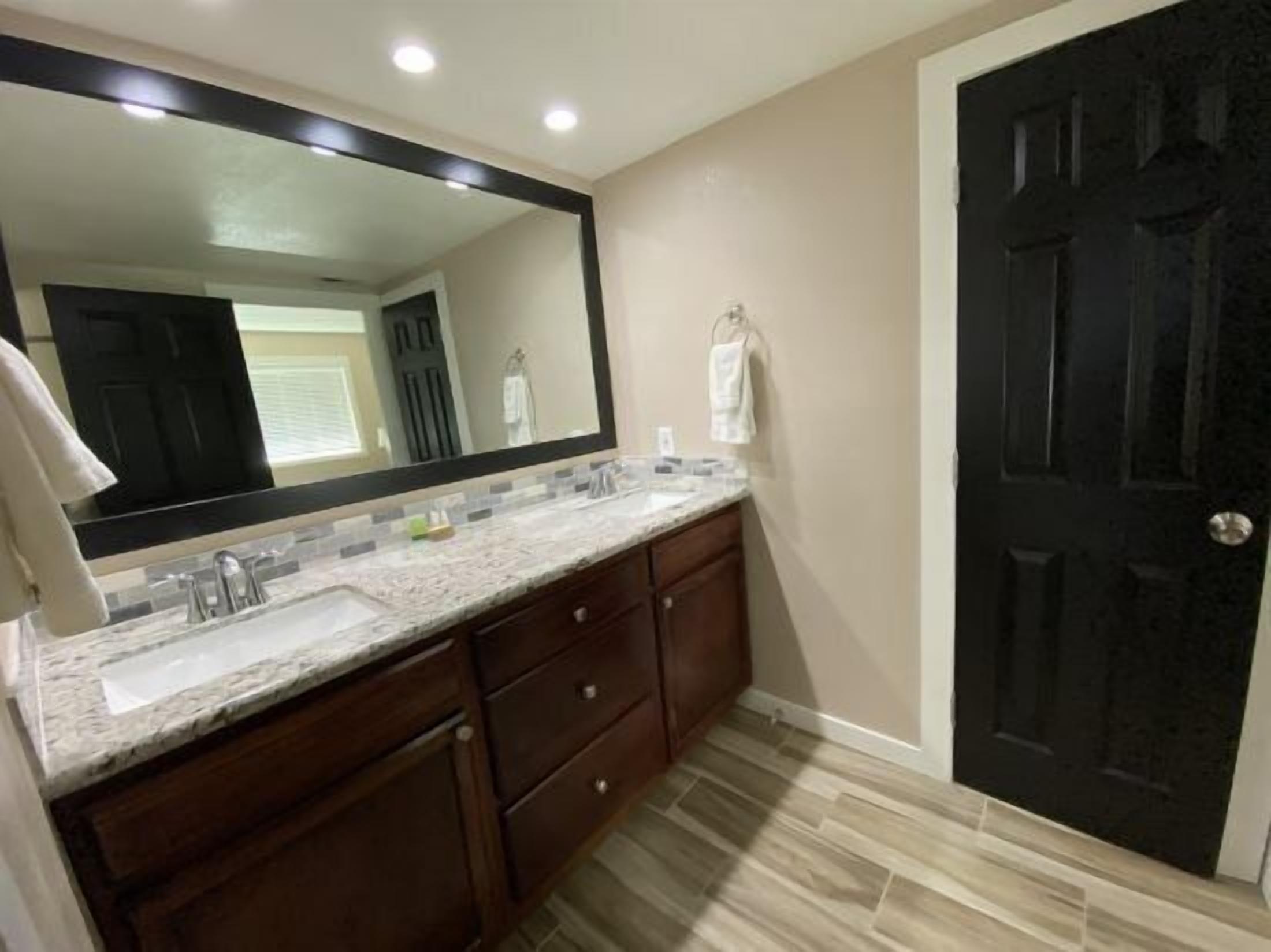 A bathroom with a large mirror, a sink, a vanity with drawers, and a dark door.