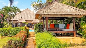 Een resort met rieten hutten, een zwembad en weelderige begroeiing.