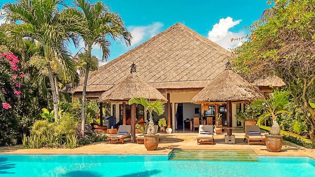 Een resort met een zwembad, ligbedden en hutten met rieten daken.