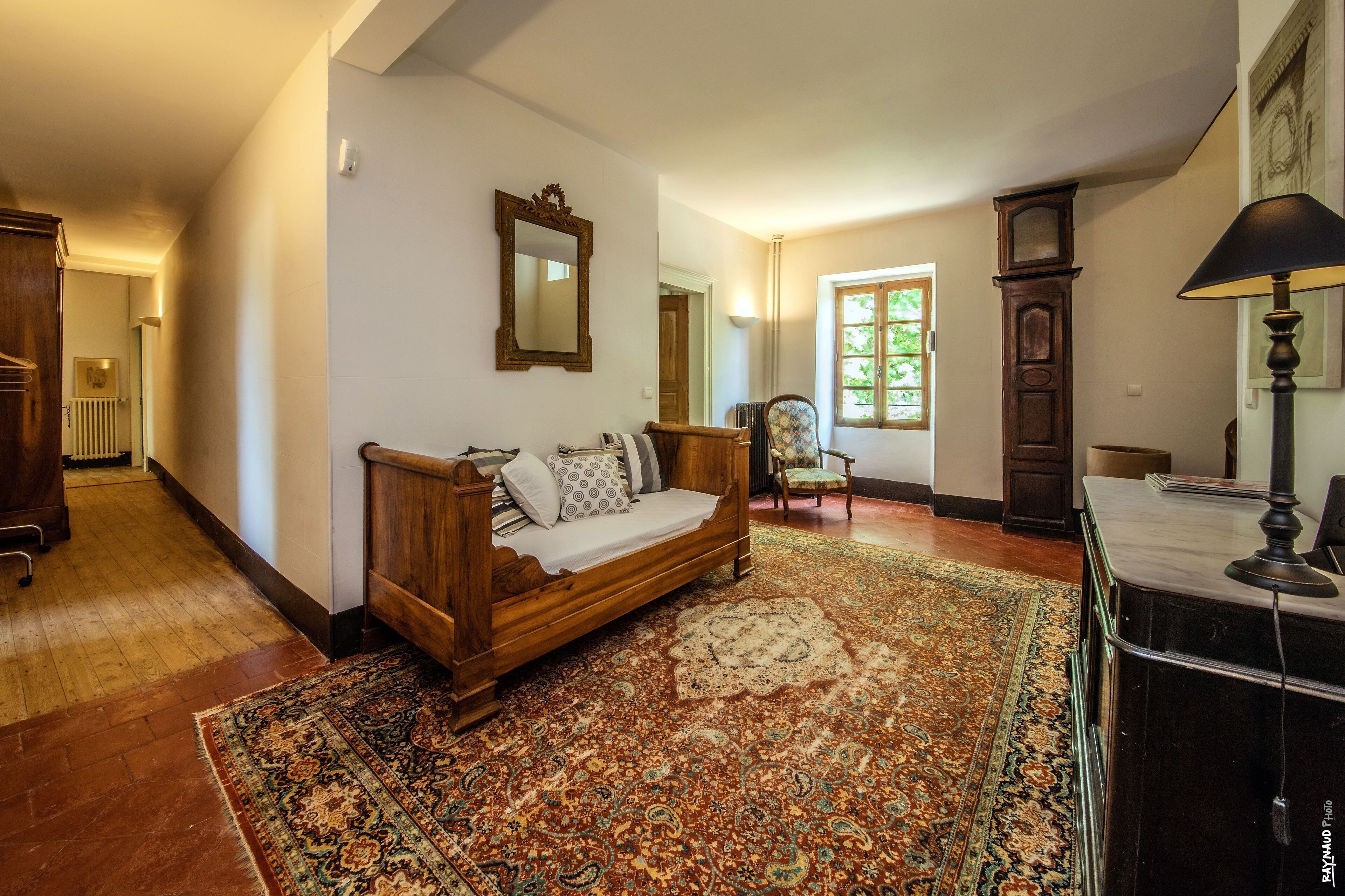 A traditional room with a wooden bed, a patterned rug, a wooden chair, and a desk with a lamp.