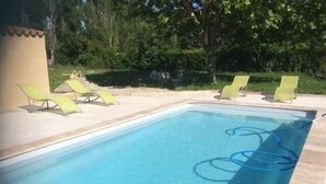 Une piscine rectangulaire à l’eau d’un bleu limpide, entourée d’une terrasse carrelée. Plusieurs chaises longues vertes sont alignées le long du bord de la piscine.