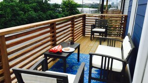 A wooden deck with outdoor furniture, including chairs and a table, and a view of greenery in the background.
