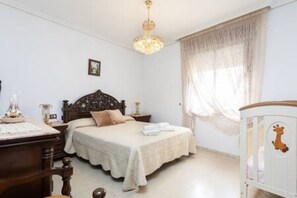 A bedroom with a bed, a nightstand, a dresser, and a window with sheer curtains.