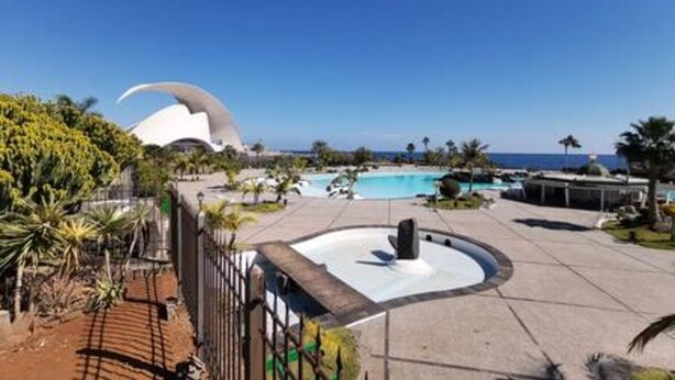 A resort with a pool, palm trees, and a distinctive white building with a curved roof. - Home2Book Spacious Classic Design Apto SC Center (Santa Cruz de Tenerife)