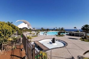 A resort with a pool, palm trees, and a distinctive white building with a curved roof.