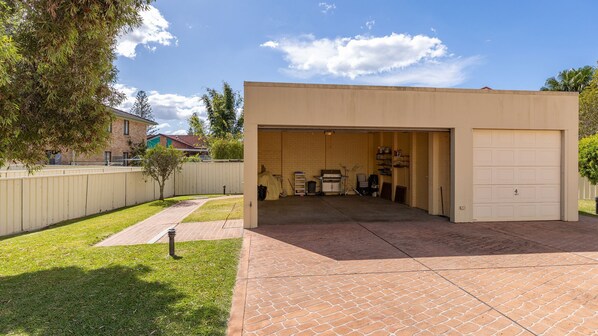 A garage with a brick patio leading to it, a covered outdoor area with barbecue equipment, and a fenced yard. - Castillo Del Mar 10 - Overlooking the Lake (Tuncurry)