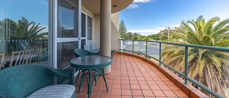 Uma varanda com mesa e cadeiras, porta de vidro e vista para palmeiras.