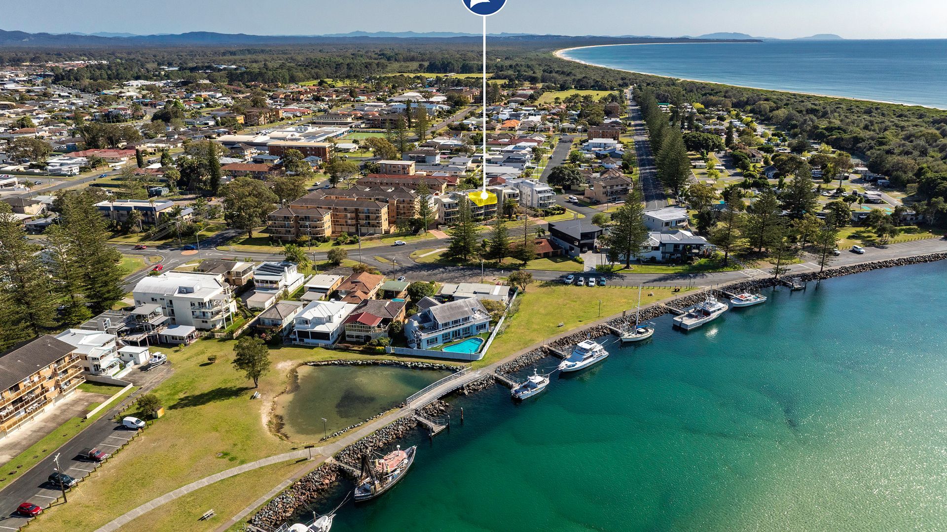 An aerial view of a coastal residential area with houses, a marina, and a clear view of the ocean.
