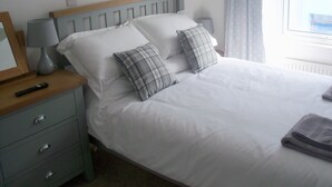 A neatly made bed with white linens and plaid pillows, a bedside table with a lamp, and a folded towel on the bed.