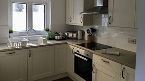 A modern kitchen with white cabinetry, a stainless steel range hood, a built-in oven, and a window providing natural light.
