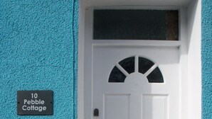 A white door with a small window above it, a mailbox to the left, and a sign reading "10 Pebble Cottage" on the wall.