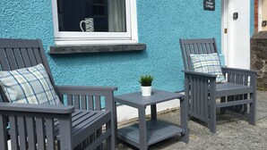 Two grey wooden chairs with plaid cushions, a small white table, and a potted plant.