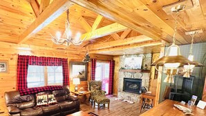 Interior acogedor de una cabaña de troncos con chimenea, mobiliario de cuero y una mesa de comedor de madera.