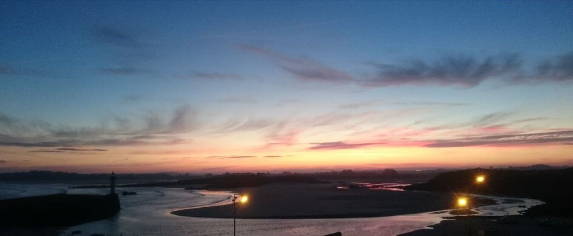 Un atardecer sobre un río con una isla circular y dos luces en la orilla.