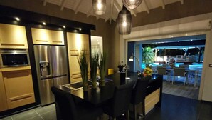 Une cuisine moderne dotée d’appareils électroménagers en acier inoxydable, un coin repas avec des chaises noires et une vue sur une piscine extérieure.