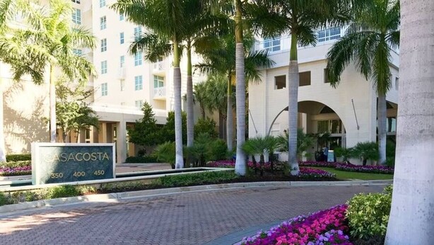 A hotel entrance with a sign reading "CASACOSTA" and a landscaped area with flowers. - One bedroom in amazing luxury condo. BEACH PASS INCLUDED! (Boynton Beach)
