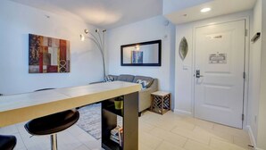A modern living room with a dining table, a sofa, a decorative plant, and a door with a 'No Smoking' sign. - One bedroom in amazing luxury condo. BEACH PASS INCLUDED! (Boynton Beach)