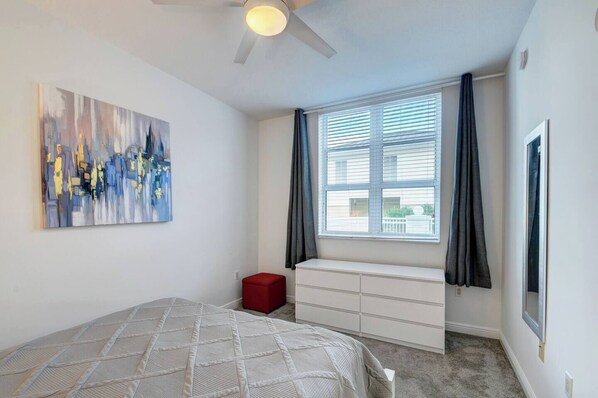 Un dormitorio con cama, una ventana con cortinas, un aparador blanco y un ventilador de techo.