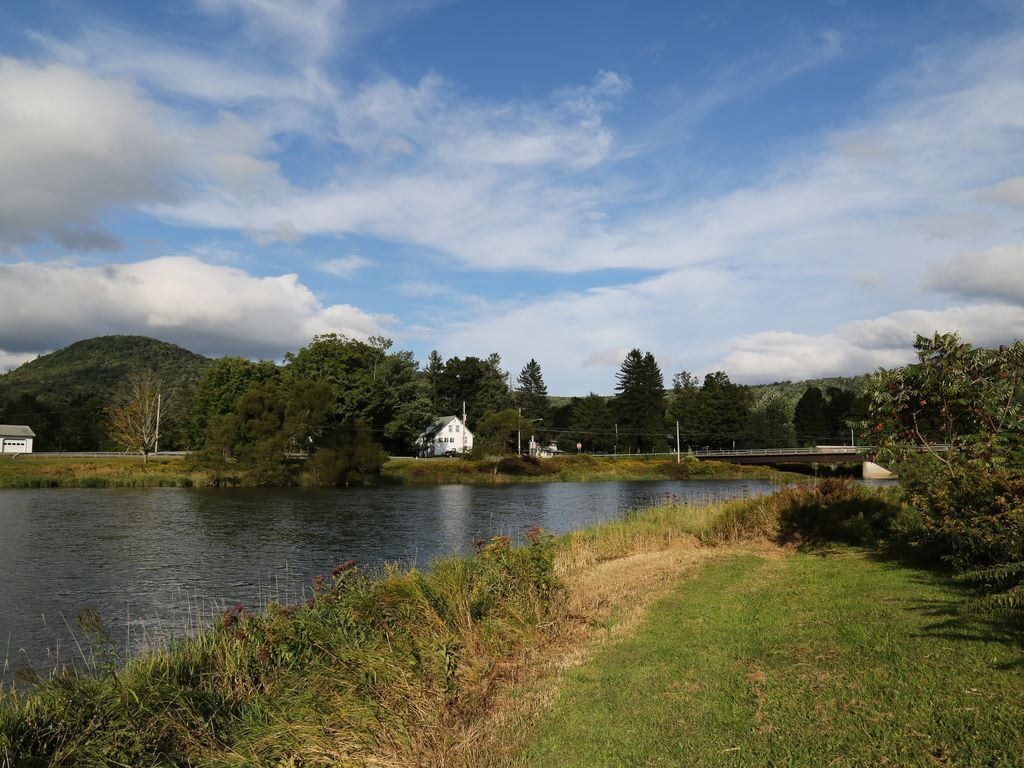 A serene lakeside view with a white house, a bridge, and lush greenery.