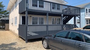 A two-story building with a balcony, a car parked in front, and a clear sky. - Oceanside Duplex, 7 houses to beach; 2nd floor (Long Beach Township)