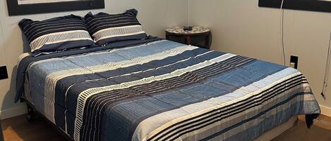 A bedroom with a bed, two windows, a bedside table, and a wall-mounted air conditioner.