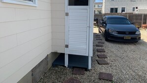 A compact, single-story building with a white exterior, a small door, and a gravel driveway. - Oceanside Duplex, 7 houses to beach; 2nd floor (Long Beach Township)