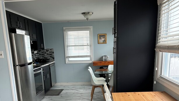 A compact kitchen with modern appliances, a dining area with a wooden table and chairs, and a window with blinds. - Oceanside Duplex, 7 houses to beach; 2nd floor (Long Beach Township)
