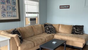 A living room with a beige sectional sofa, a small black coffee table, and a framed marine life artwork on the wall. - Oceanside Duplex, 7 houses to beach; 2nd floor (Long Beach Township)