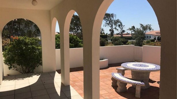 Eine überdachte Terrasse im Freien mit Bögen, einem runden Steintisch und Topfpflanzen.