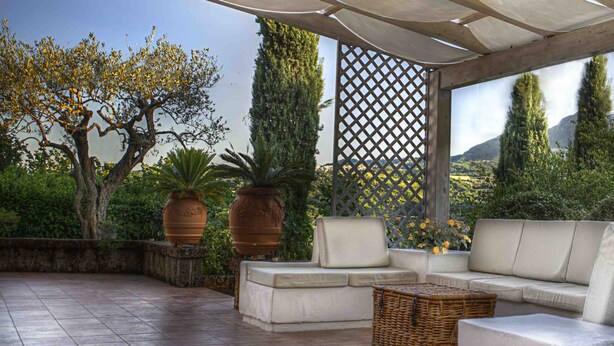 A covered outdoor seating area with a sofa and chairs, surrounded by potted plants and a view of the landscape. - SARKEEP - Villa immersed in the Taurasi vineyards (Luogosano)