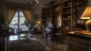 A cozy room with a large wooden bookshelf, a desk with a laptop, wicker furniture, and a patterned rug. - SARKEEP - Villa immersed in the Taurasi vineyards (Luogosano)