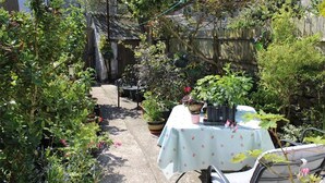 Une terrasse de jardin avec une table et des chaises, entourée de plantes en pot et d’une clôture en bois.