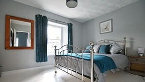 Une chambre à coucher avec un lit à ossature métallique, un grand miroir et une fenêtre avec des rideaux.