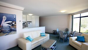 A living room with a sofa, a coffee table, and a dining area with chairs. There is a kitchen area with cabinets and appliances. - Horizons 1 - Location, location, location! (Forster)