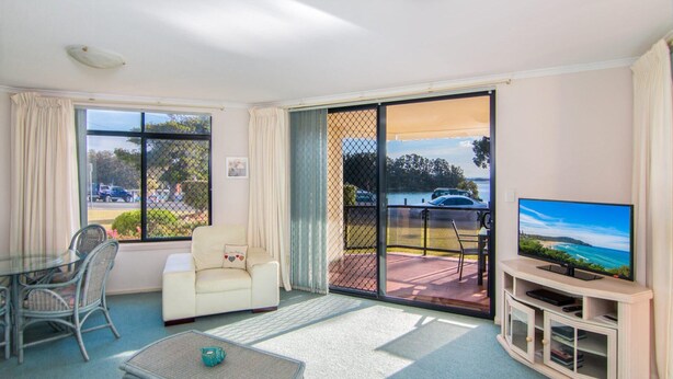A living room with a sofa, a glass coffee table, a TV, and a view of a lake and cars through the sliding glass door. - Horizons 1 - Location, location, location! (Forster)