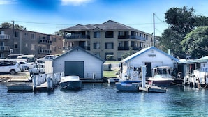 A marina with several boats docked, a small building with a gabled roof, and a larger building with multiple windows in the background. - Horizons 1 - Location, location, location! (Forster)