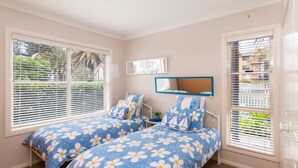 Une chambre avec deux lits, chacun agrémenté de draps à motifs floraux bleus, un radiateur blanc et une fenêtre avec des stores.