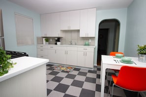 Una cocina con armarios blancos, piso de cuadros, una mesa de comedor con un tazón verde y una silla roja.