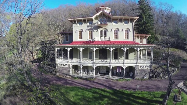 A large, two-story house with a red roof and white trim, surrounded by trees.
