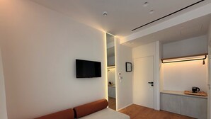 A modern hotel room with a flat-screen TV, a sofa, a bed, a wooden floor, and a kitchenette area. - Villa Mucho (Sarandë)