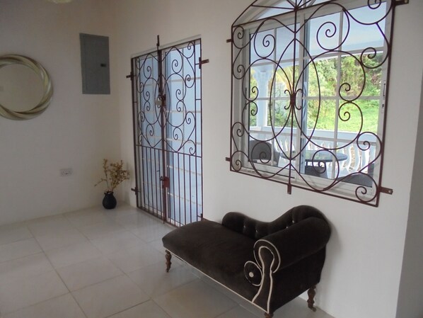 Une pièce avec un canapé noir, une grille en métal décorative et une fenêtre donnant sur un jardin.