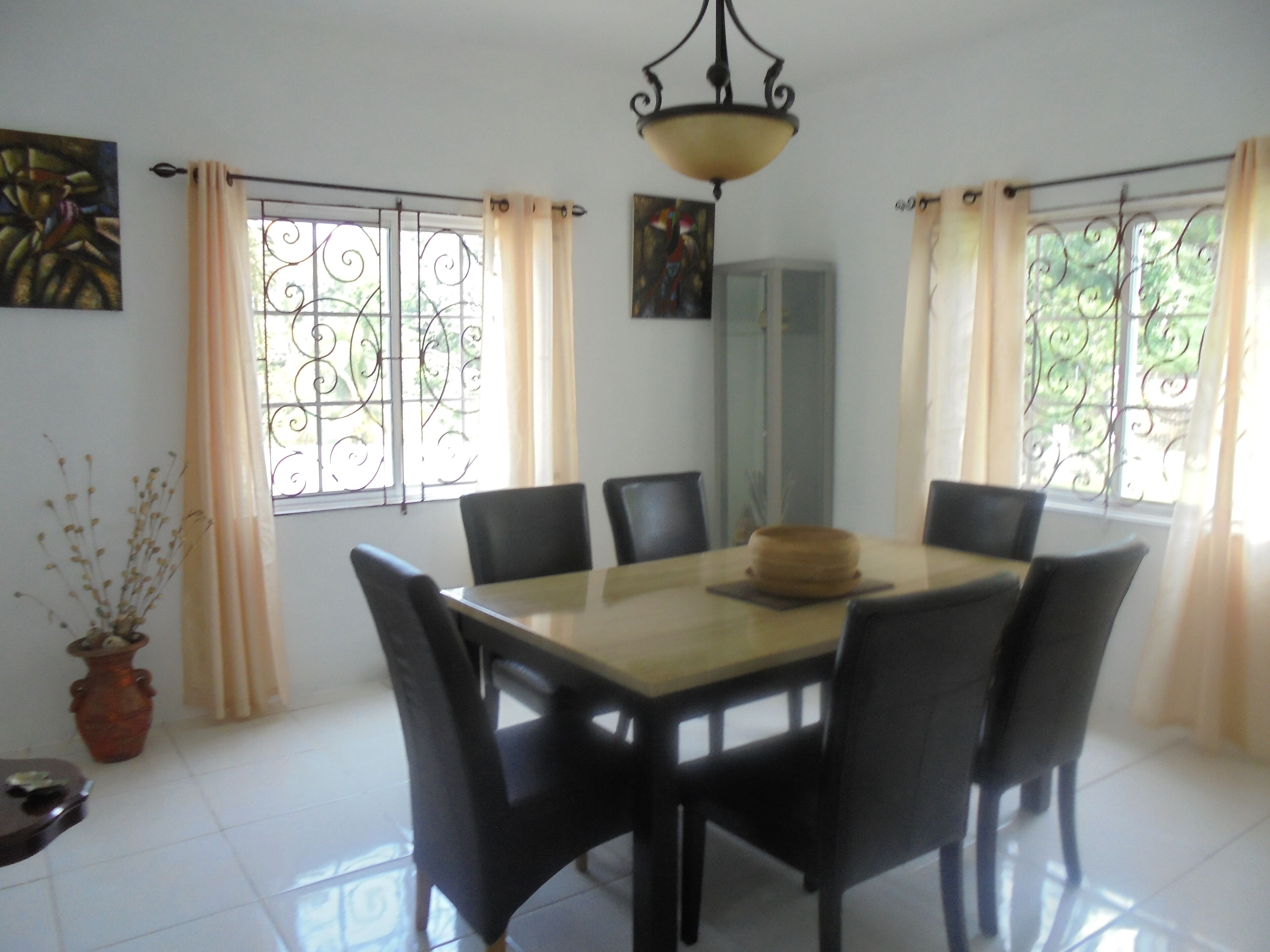 A dining area with a round table, six chairs, and a chandelier.