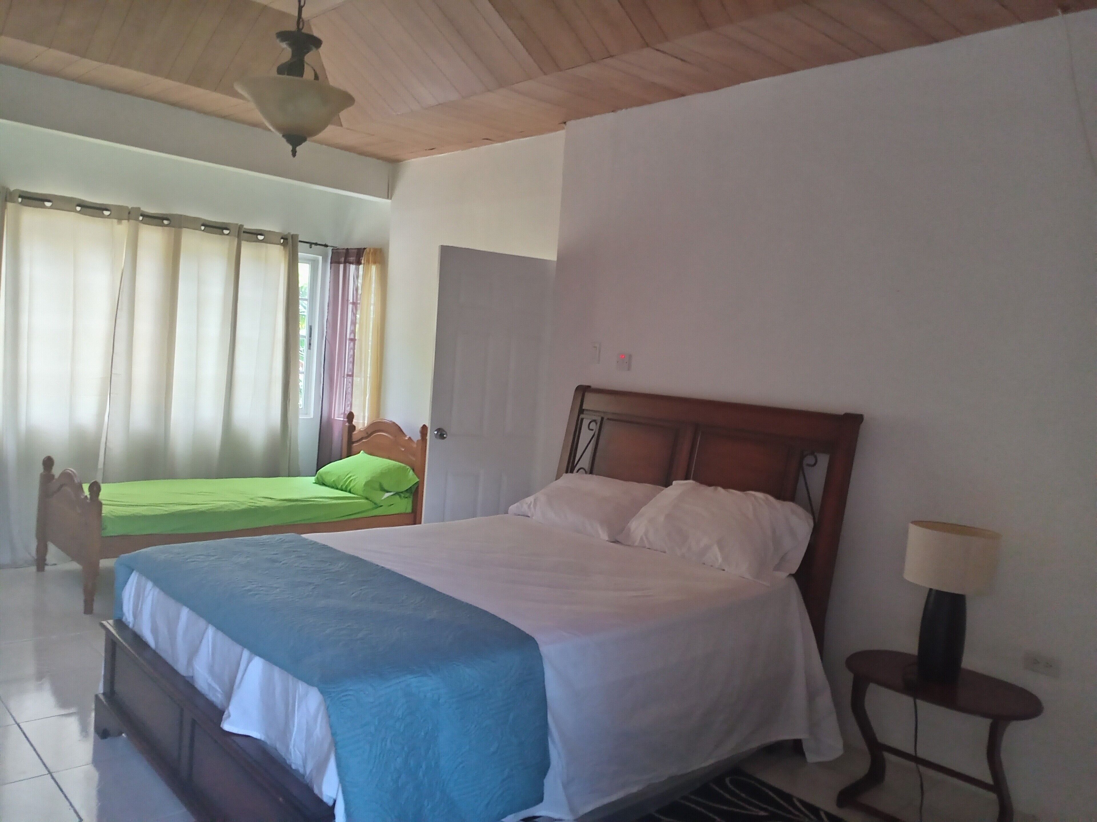 Un dormitorio con una cama grande, una cama más pequeña, techo de madera y una ventana con cortinas.