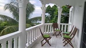 A balcony with white balustrades, three wooden chairs with green cushions, and a solar panel on the wall. - Pearl Ocean Villa (Saint Margarets Bay)