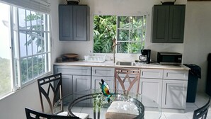 A kitchen with white cabinets, a microwave, a coffee maker, and a window with a view of greenery. - Pearl Ocean Villa (Saint Margarets Bay)