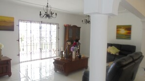 A spacious living room with a large window, a chandelier, a sofa, and a wooden cabinet. - Pearl Ocean Villa (Saint Margarets Bay)