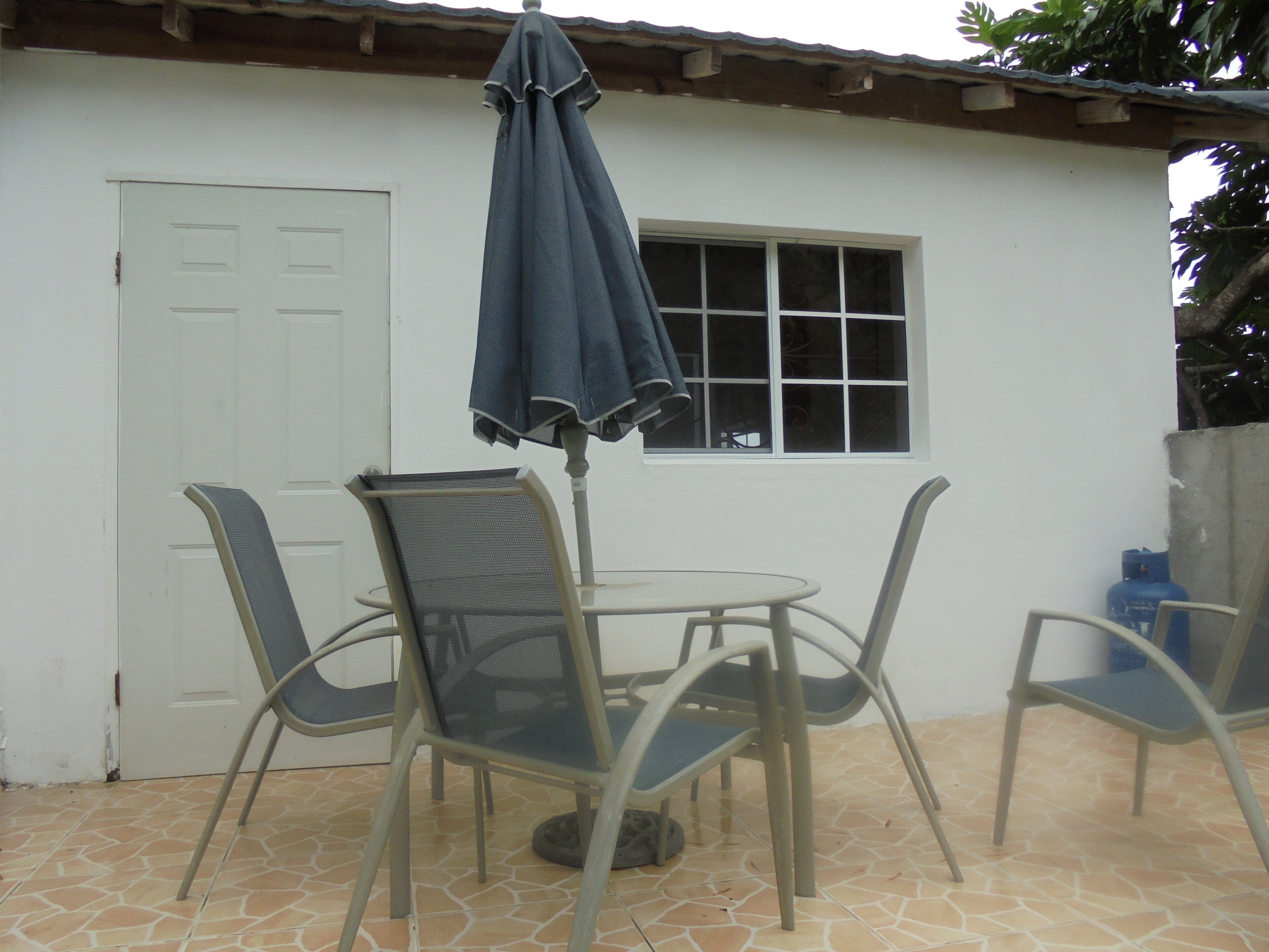 Un patio al aire libre con una mesa, cuatro sillas, una sombrilla y una puerta blanca.