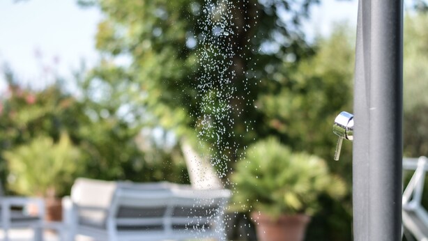 A water feature with water droplets in mid-air, a white outdoor seating area, and potted plants in the background. - Very nice 'villetta' in beautiful and quiet fully garden. (Bardolino)